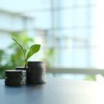 A small plant sprouting from stacked silver coins, symbolizing growth in finance.